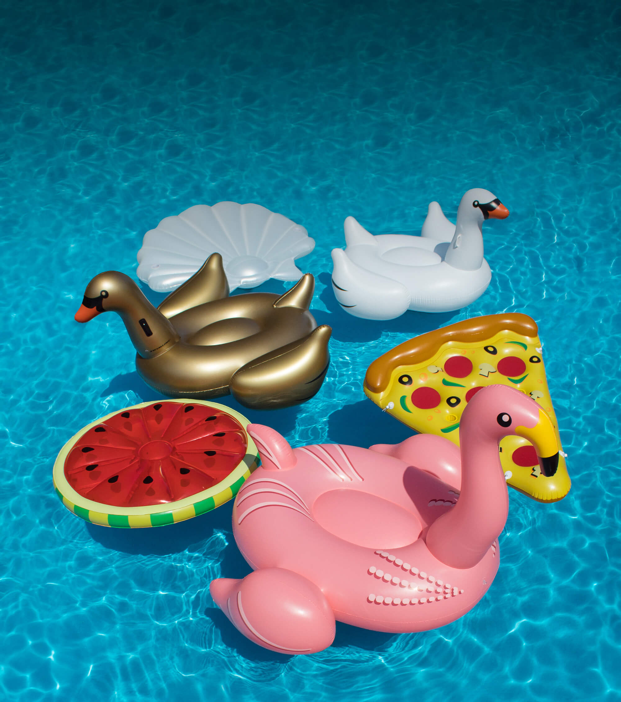 Inflatable pool toys including swans, a pizza slice, watermelon, and a shell on a blue pool background.